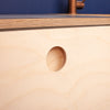 Close-up of a round hole in a light B/BB grade birch plywood board, typically part of a plyzen Corner Doors piece or a craft project, against a blue fabric background.